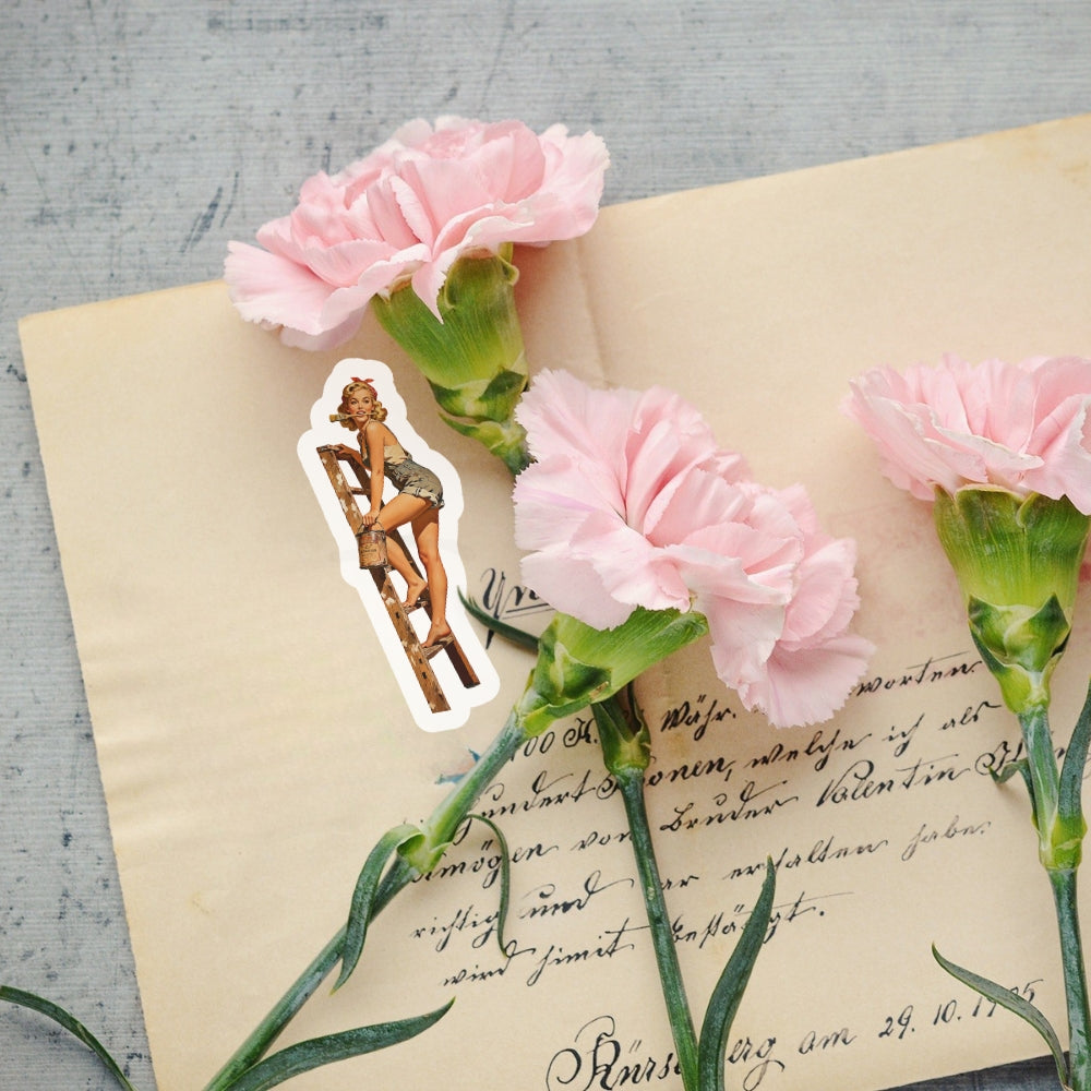 Pink carnations on an old letter with a small sticker of a woman on a ladder.