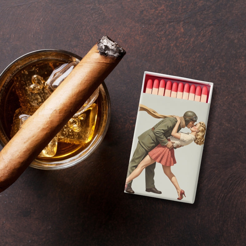 Cigar in an ashtray with a matchbox featuring vintage artwork on a dark surface