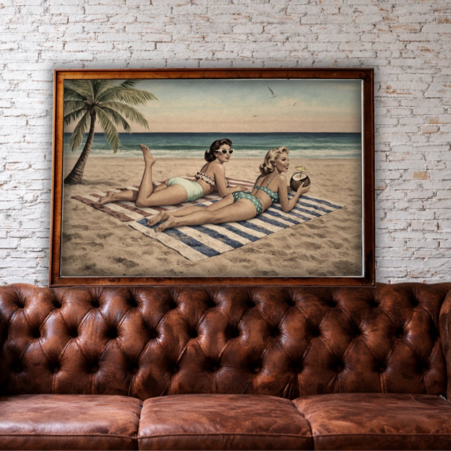 Framed artwork of two women on a beach with a palm tree, displayed above a brown leather sofa against a brick wall.