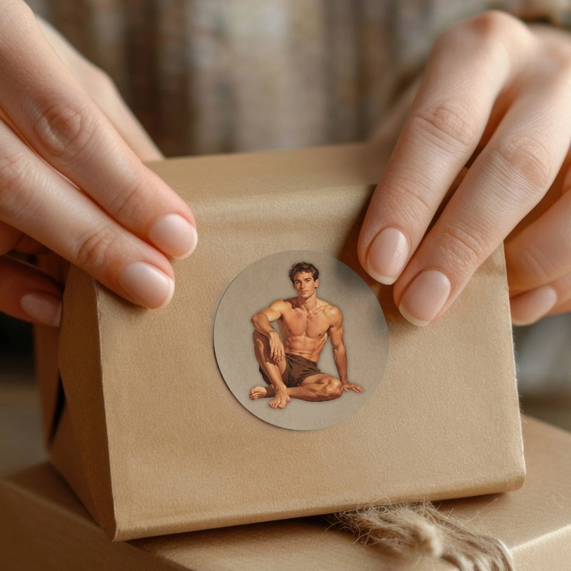 Person holding a brown paper box with a circular sticker featuring a shirtless man on a neutral background