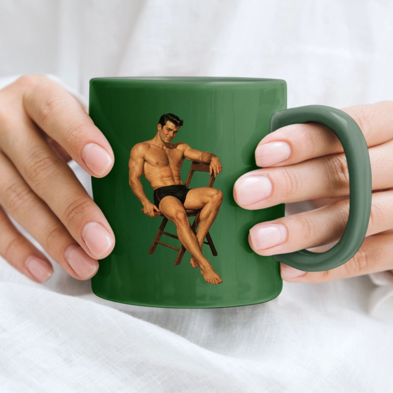 Green mug with a graphic of a shirtless man on a chair held by two hands.