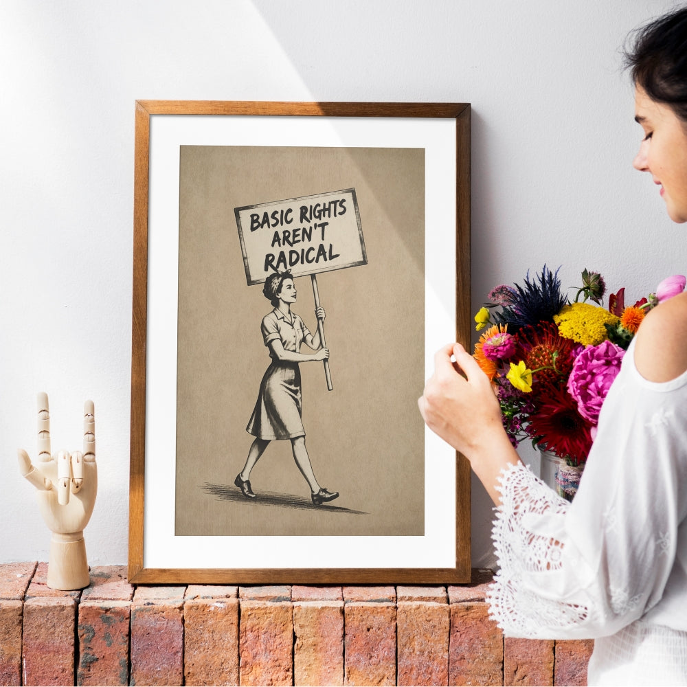 Framed artwork with a woman holding a sign reading 'Basic Rights Aren't Radical' on a brick ledge.