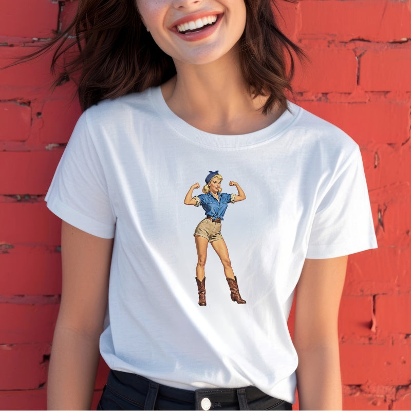 Person wearing a white t-shirt with a graphic design of a woman in a blue dress and boots against a red brick wall.