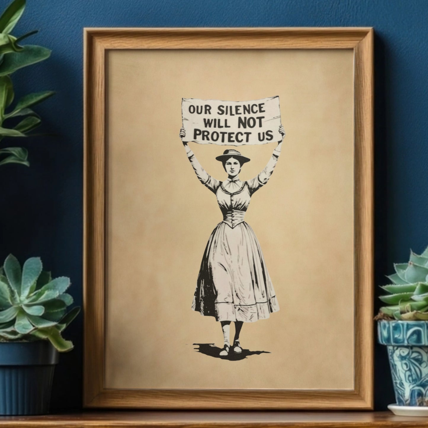 Framed artwork of a suffragist woman holding a sign with text that says, Our Silence Will NOT Protect Us, placed on a shelf with plants.