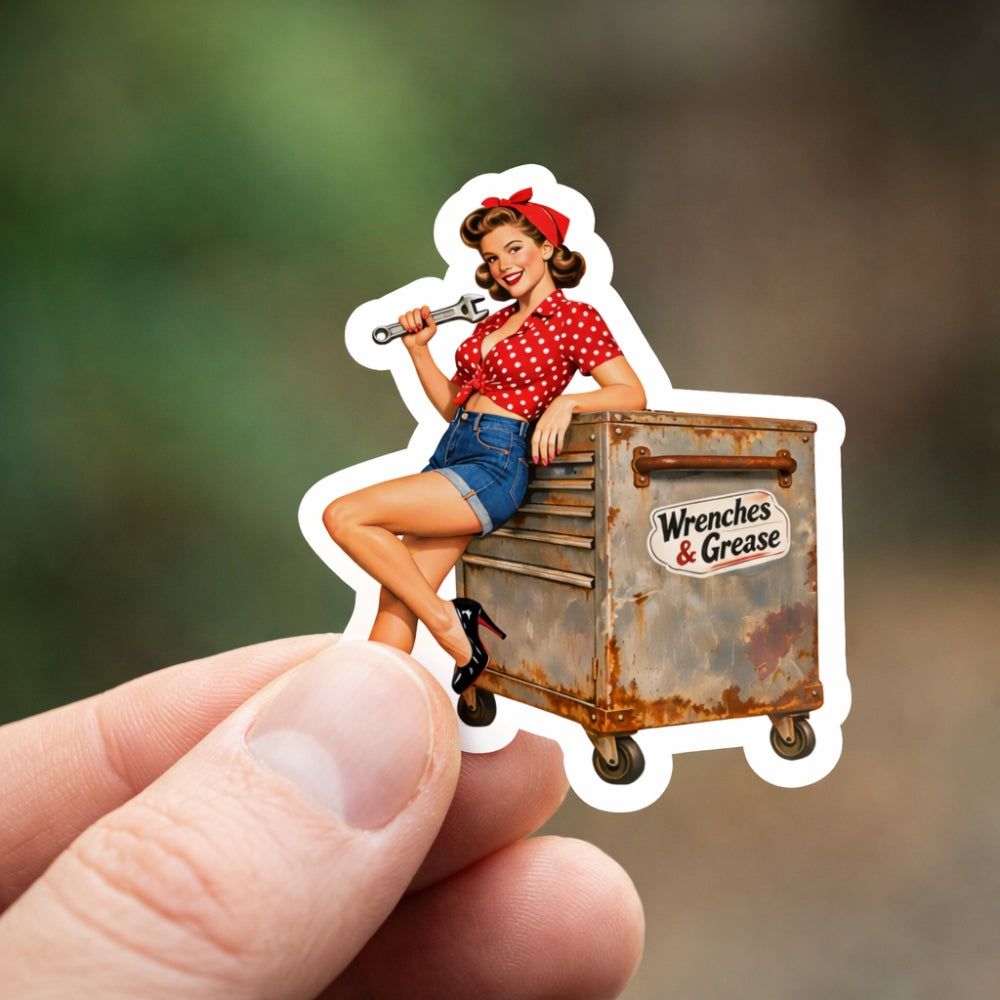 Sticker of a woman with a wrench sitting on a toolbox labeled 'Wrenches & Grease' held by a hand.