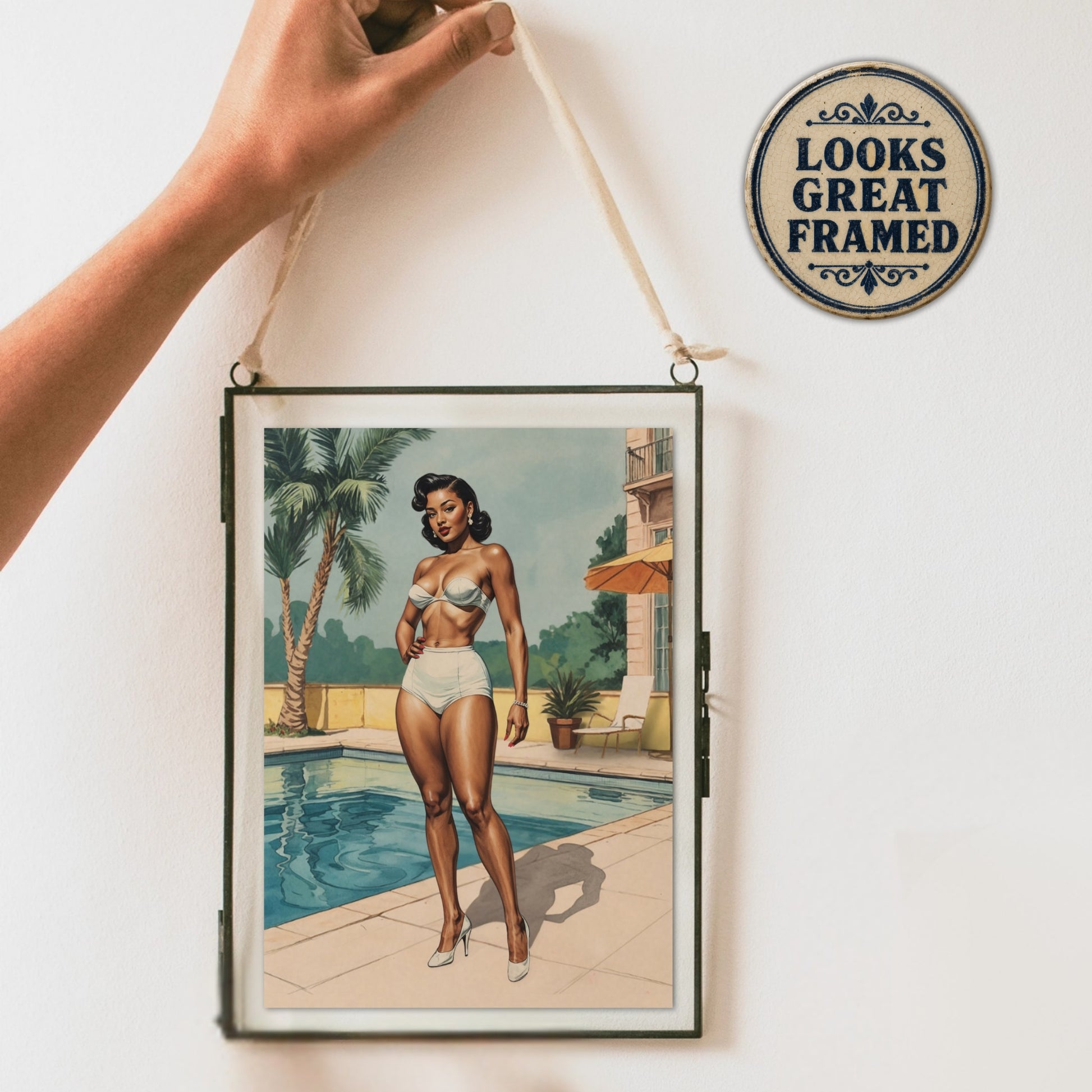 Framed artwork of a woman by a pool with a decorative sign reading 'Looks Great Framed' on a white wall.