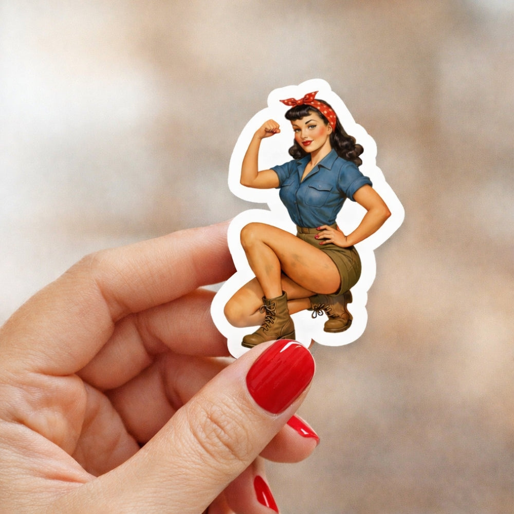 Hand holding a sticker of a vintage-style woman flexing her arm against a blurred background
