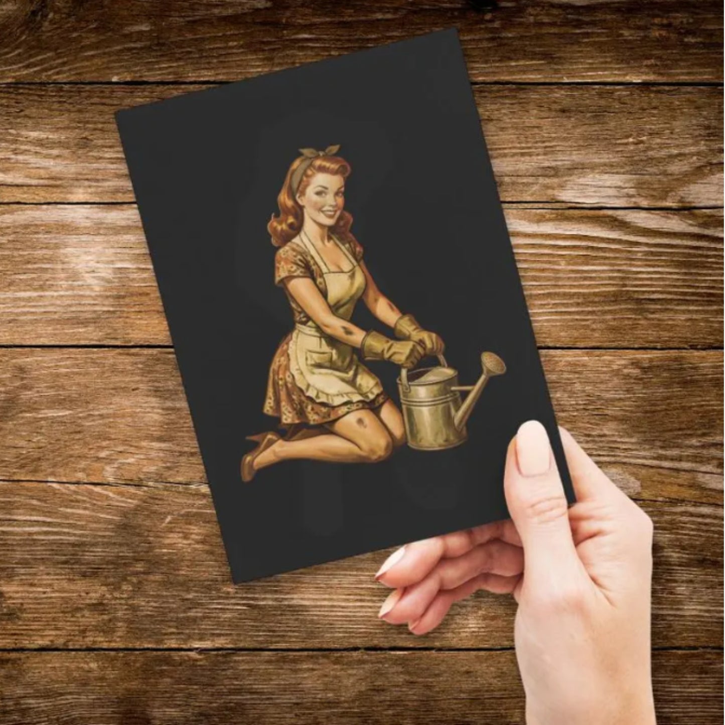 Hand holding a black card with a vintage illustration of a woman watering plants on a wooden surface.