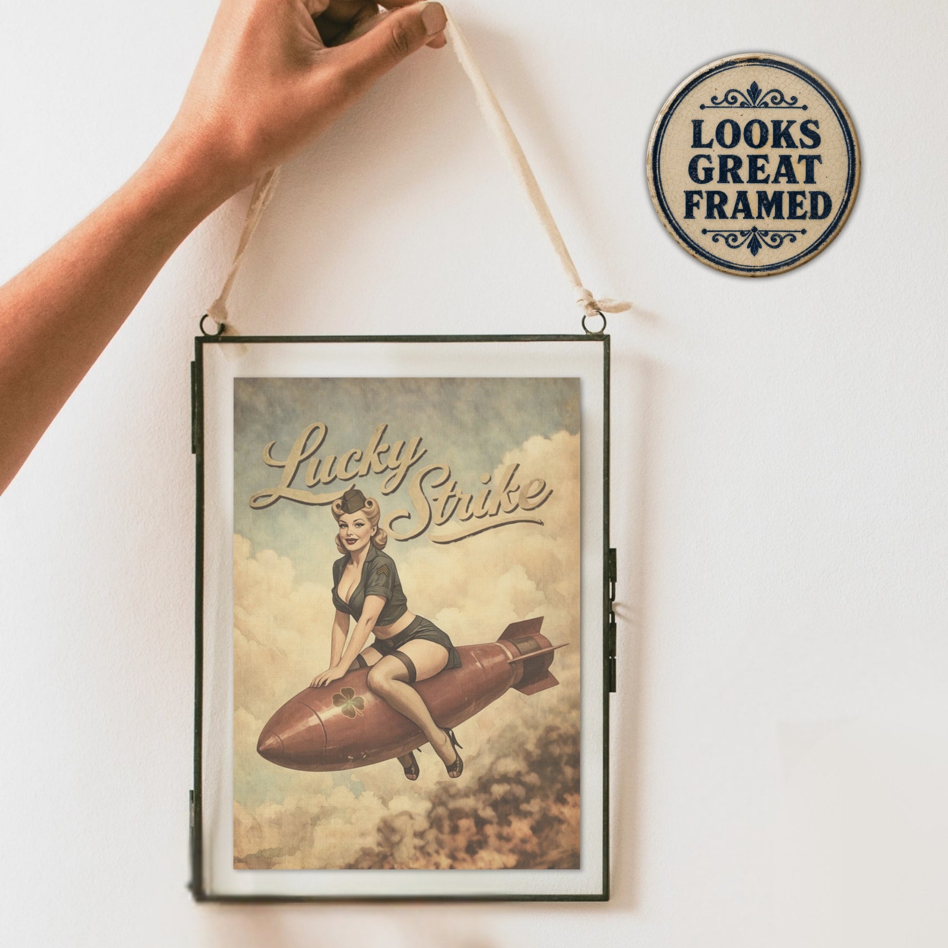 Framed poster with a vintage design of a woman on a rocket, held up against a white wall with a decorative sign.