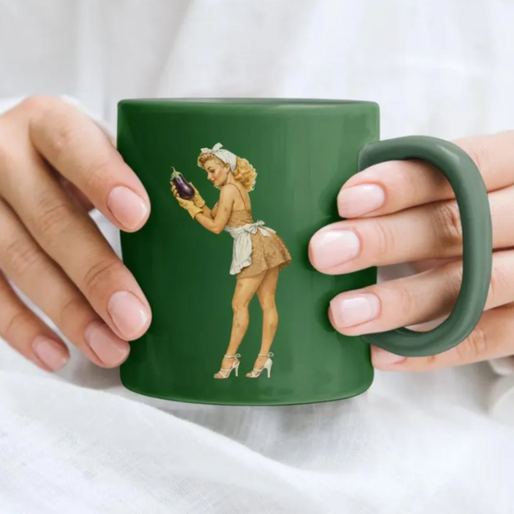 Green mug with a vintage-style illustration of a woman holding an eggplant, held by two hands.