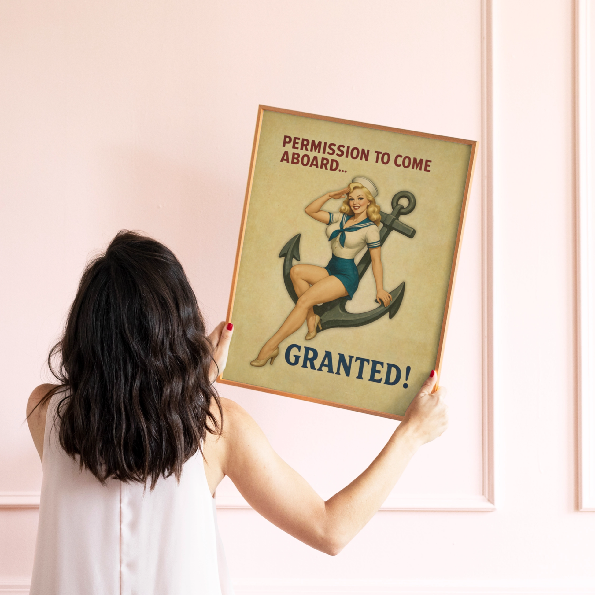 Woman holding a framed vintage-style poster with a pin-up girl and text on a pink wall.