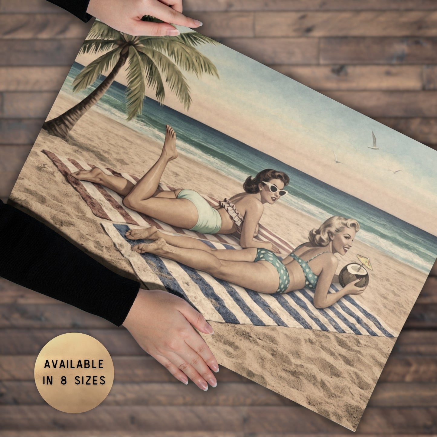 Two women in swimsuits lying on a beach with palm trees and a sailboat, held by hands on a wooden surface.