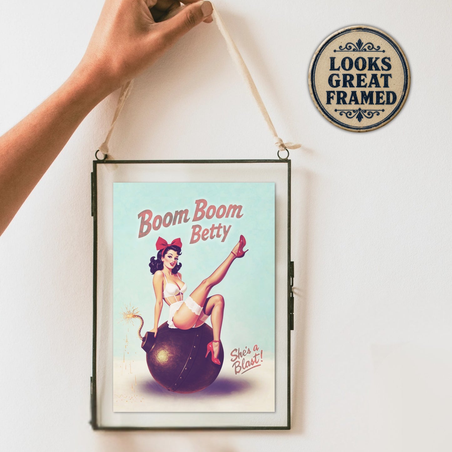Framed pinup girl card with 'Boom Boom Betty' design on a white wall with a decorative sign.