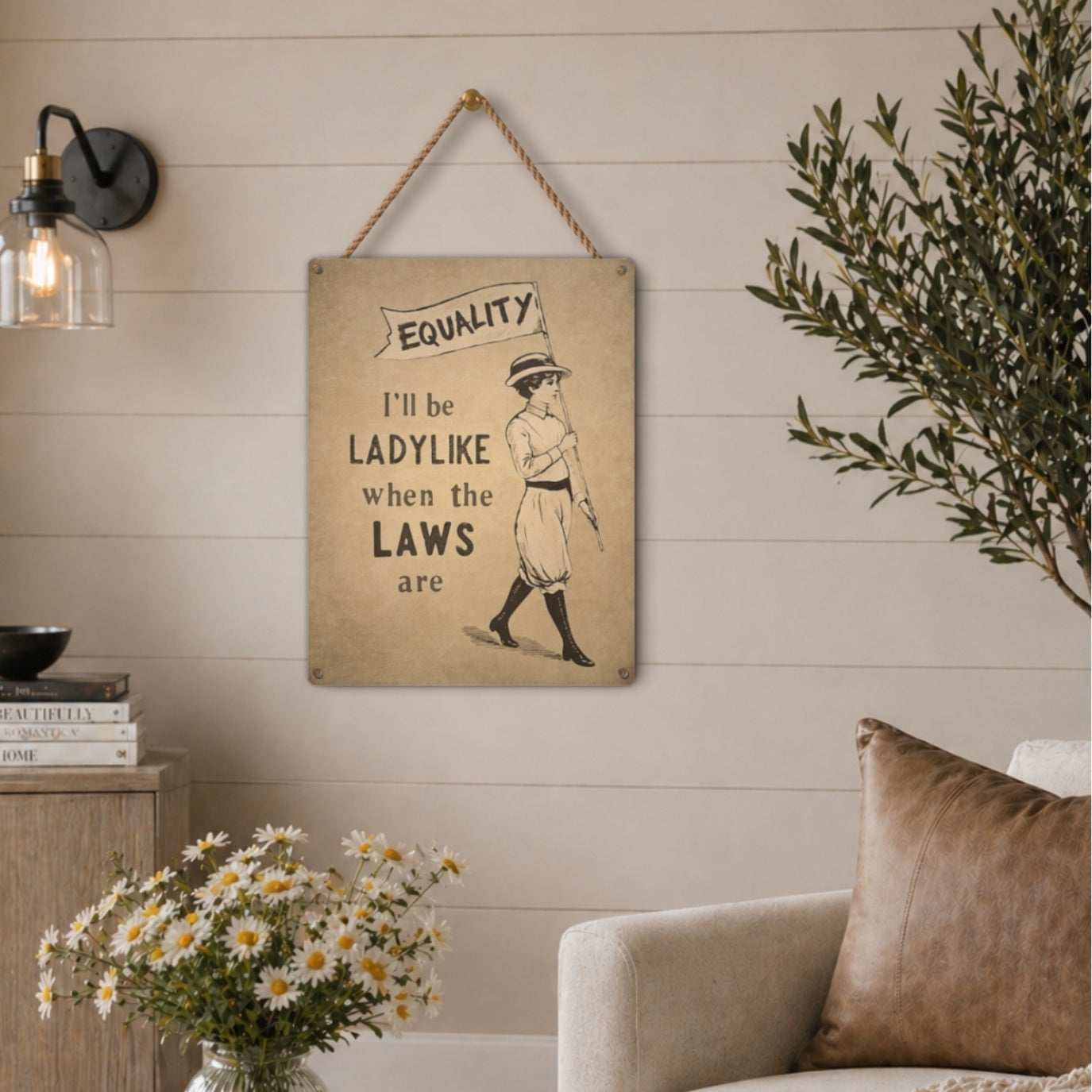 Decorative feminist sign with text and illustration of a woman, hanging on a wall in a room with a couch and flowers.