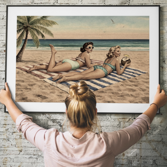 Person holding a framed artwork of two pinup women on a beach.